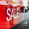Red sale sign on storefront window reflecting a busy urban street scene, capturing city life.