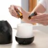 Hands preparing an essential oil diffuser with bottles for aromatherapy and wellness.